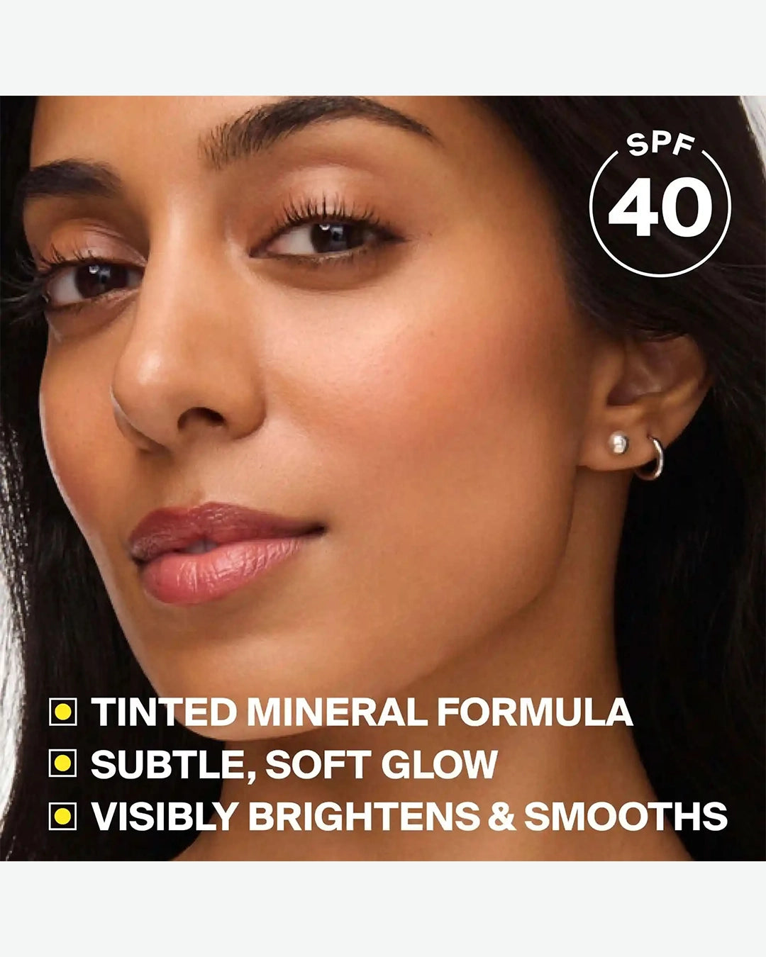 Woman's face with cosmetic product labeled SPF 40, tinted mineral formula, subtle glow, brightens, and smooths.