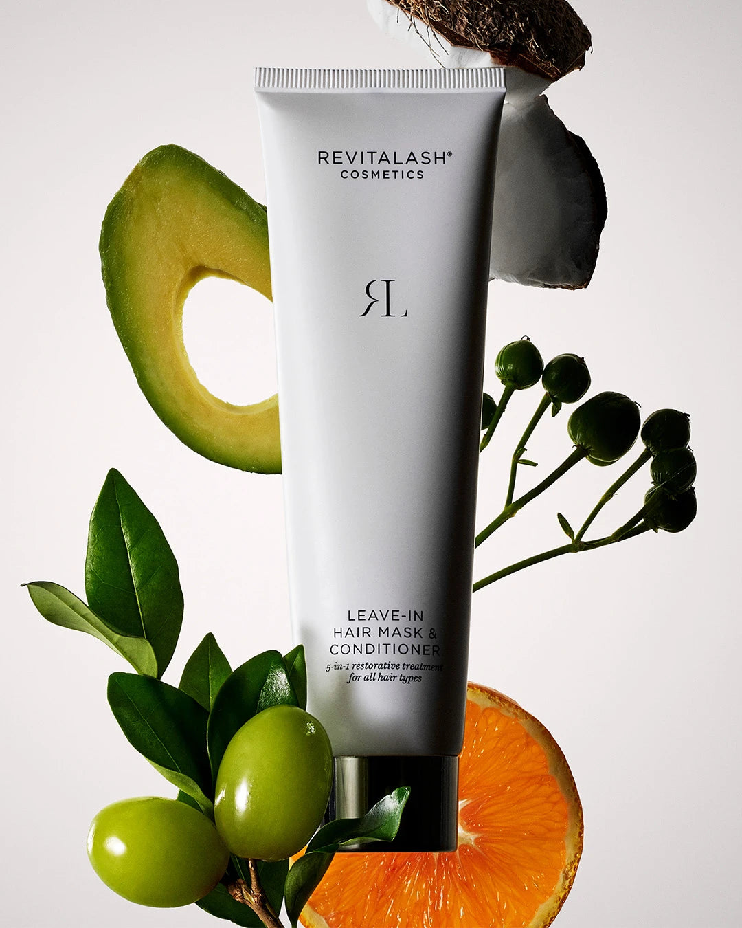Revitalash leave-in hair mask and conditioner with avocado, orange, and olive leaves on a light background
