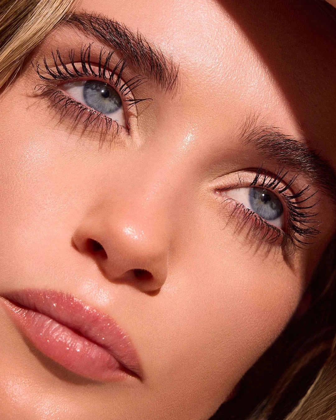 Close-up of a woman's face with blue eyes and long eyelashes, wearing a hat.