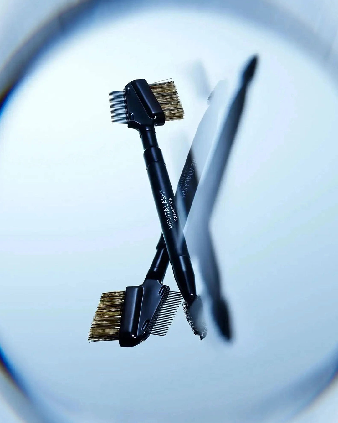 Two makeup brushes with black handles and bristle heads on a reflective surface.