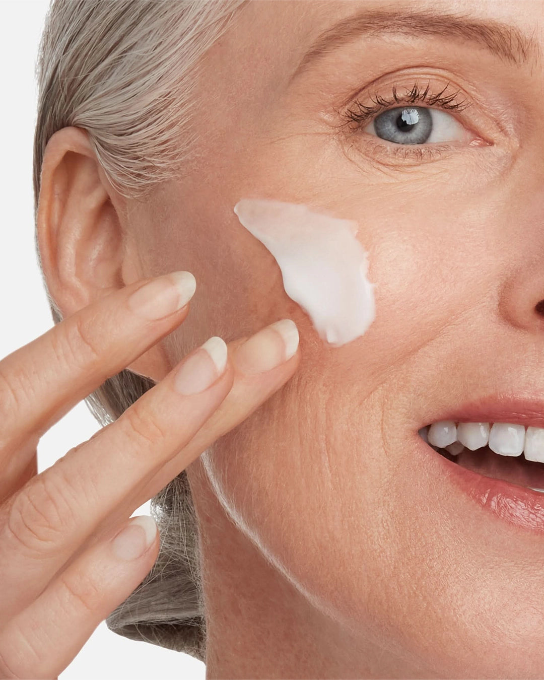 Woman applying cream to her face with a neutral background