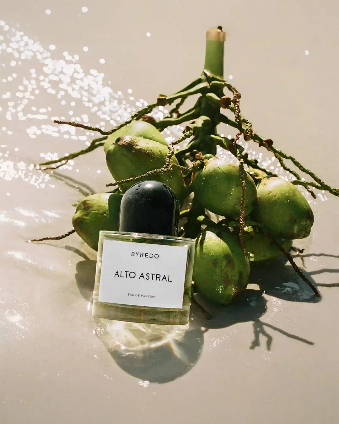 Byredo Alto Astral perfume bottle with coconuts on a shiny reflective sand surface