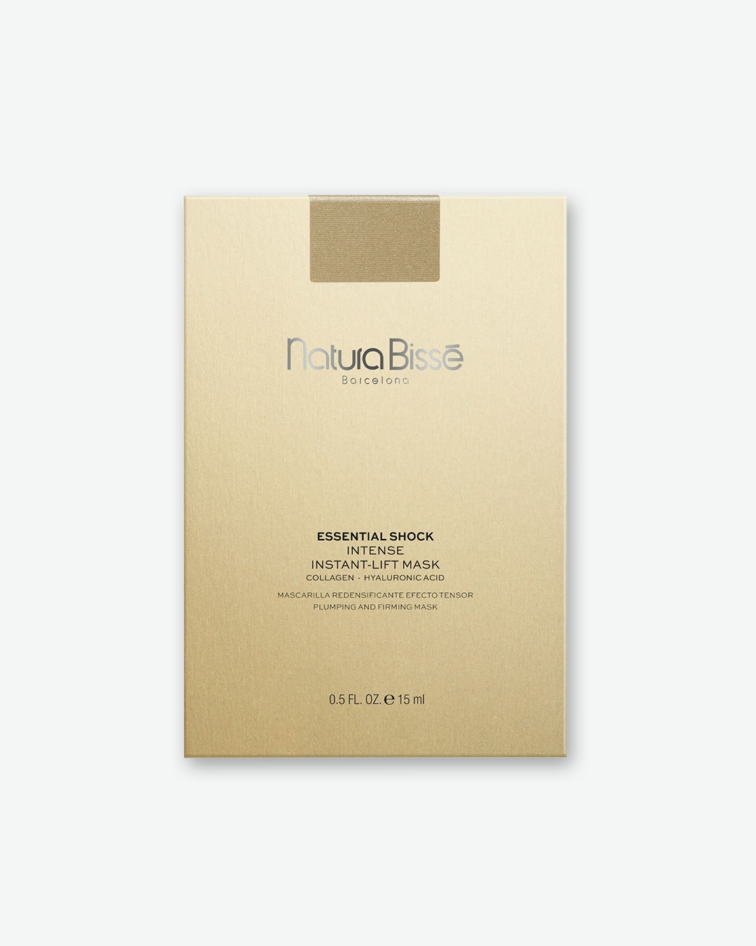 Front view of a Natura Bissé product box in a matte light-gold color with a textured finish. At the top center, there is a small rectangular metallic gold seal. The silver logo in the center reads "Natura Bissé Barcelona". Below the logo, black printed text details the product: "ESSENTIAL SHOCK INTENSE INSTANT-LIFT MASK COLLAGEN • HYALURONIC ACID", followed by "MASCARILLA REDENSIFICANTE EFECTO TENSOR PLUMPING AND FIRMING MASK". The volume "0.5 FL. OZ. e 15 ml" is printed at the very bottom against a solid w