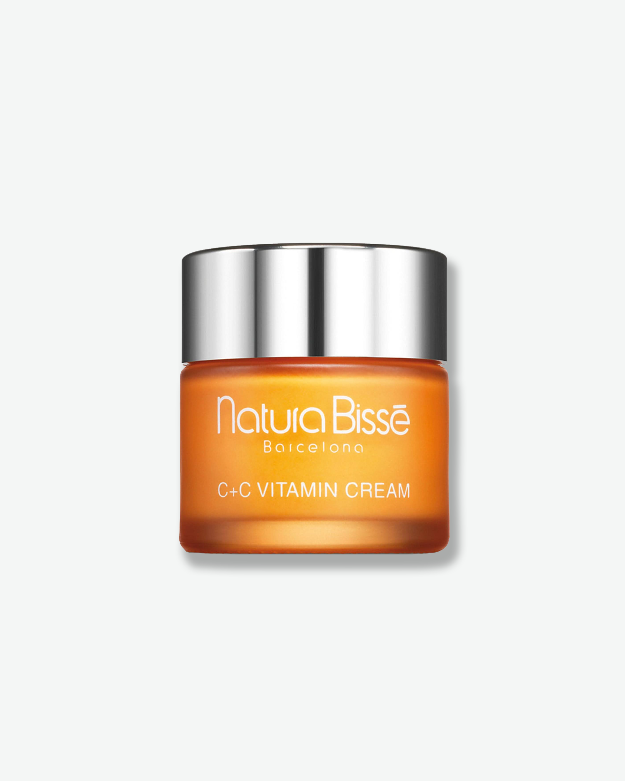 Front view of a Natura Bissé C+C Vitamin Cream jar against a plain gray background. The container features a vibrant, frosted orange glass base with white branding, capped with a reflective, polished silver lid.
