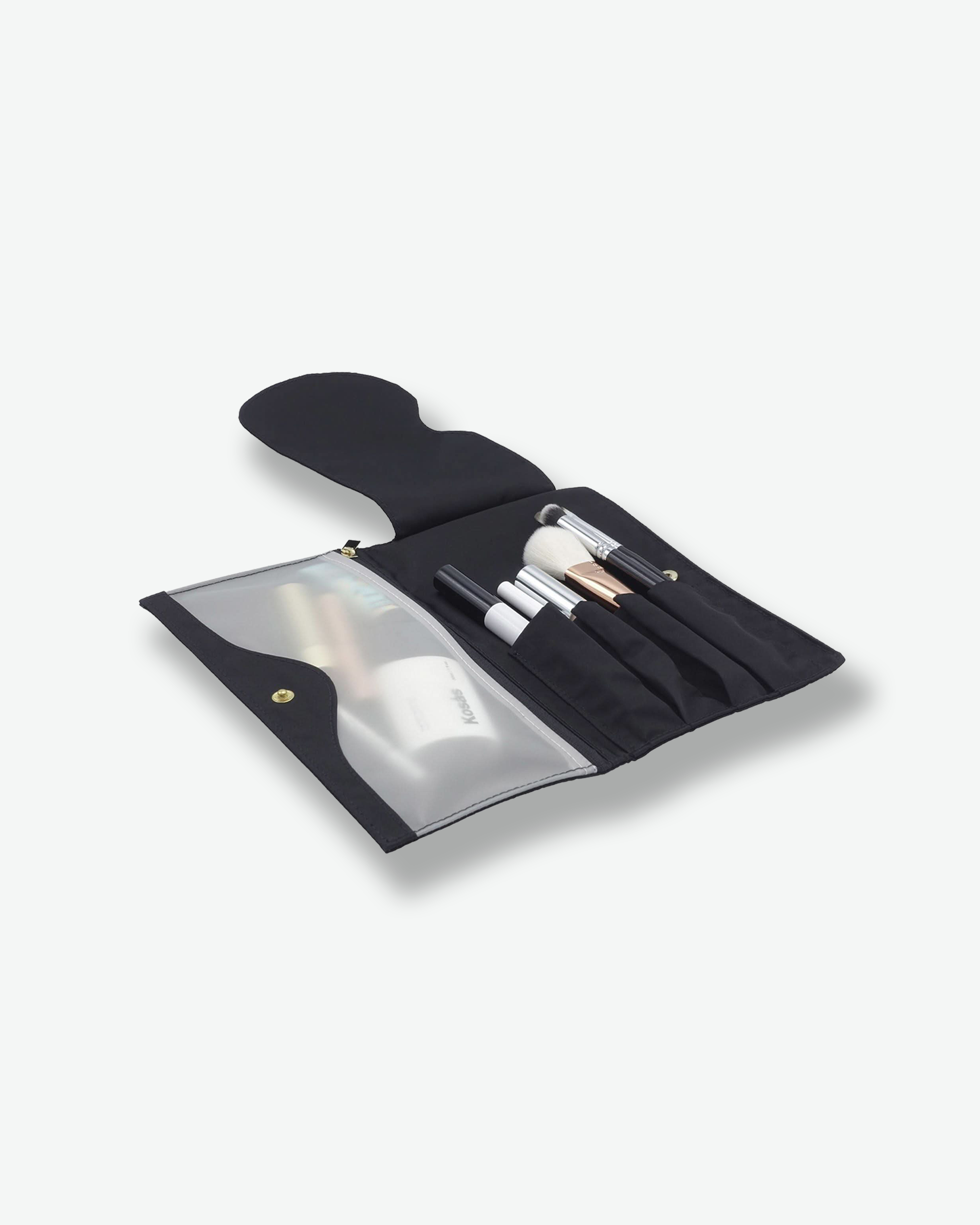 Angled view of an open black fabric makeup brush roll laid flat. The right side features specialized slots holding several cosmetic brushes, while the left side features a frosted translucent plastic zipper compartment filled with makeup products.