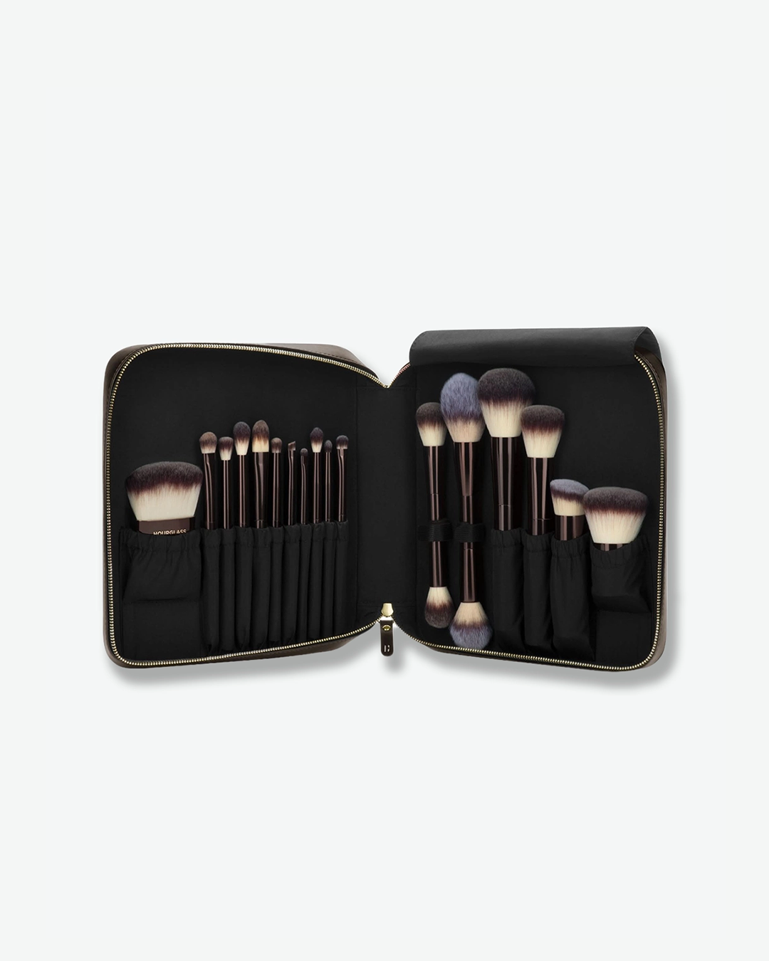 A top-down product shot of an open Hourglass makeup brush travel case lying flat against a white background. The dark brown zipped case opens like a book to reveal an assortment of professional makeup brushes with dark brown handles and dense, duo-fiber black-and-white bristles neatly organized into elastic slots on both sides.