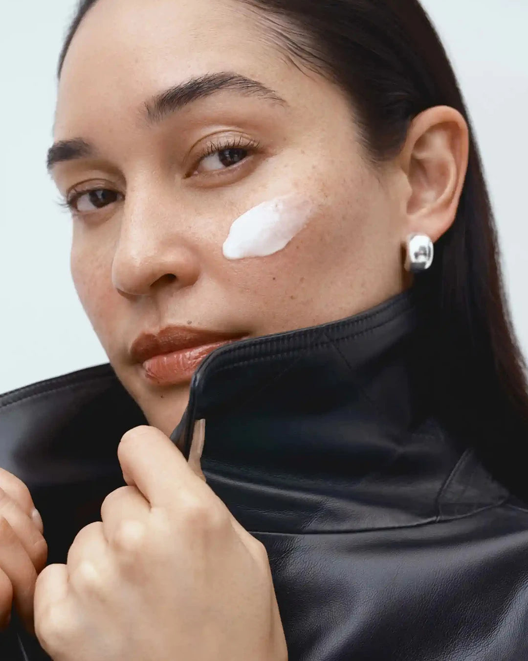 Woman applying cream to her face with a neutral background