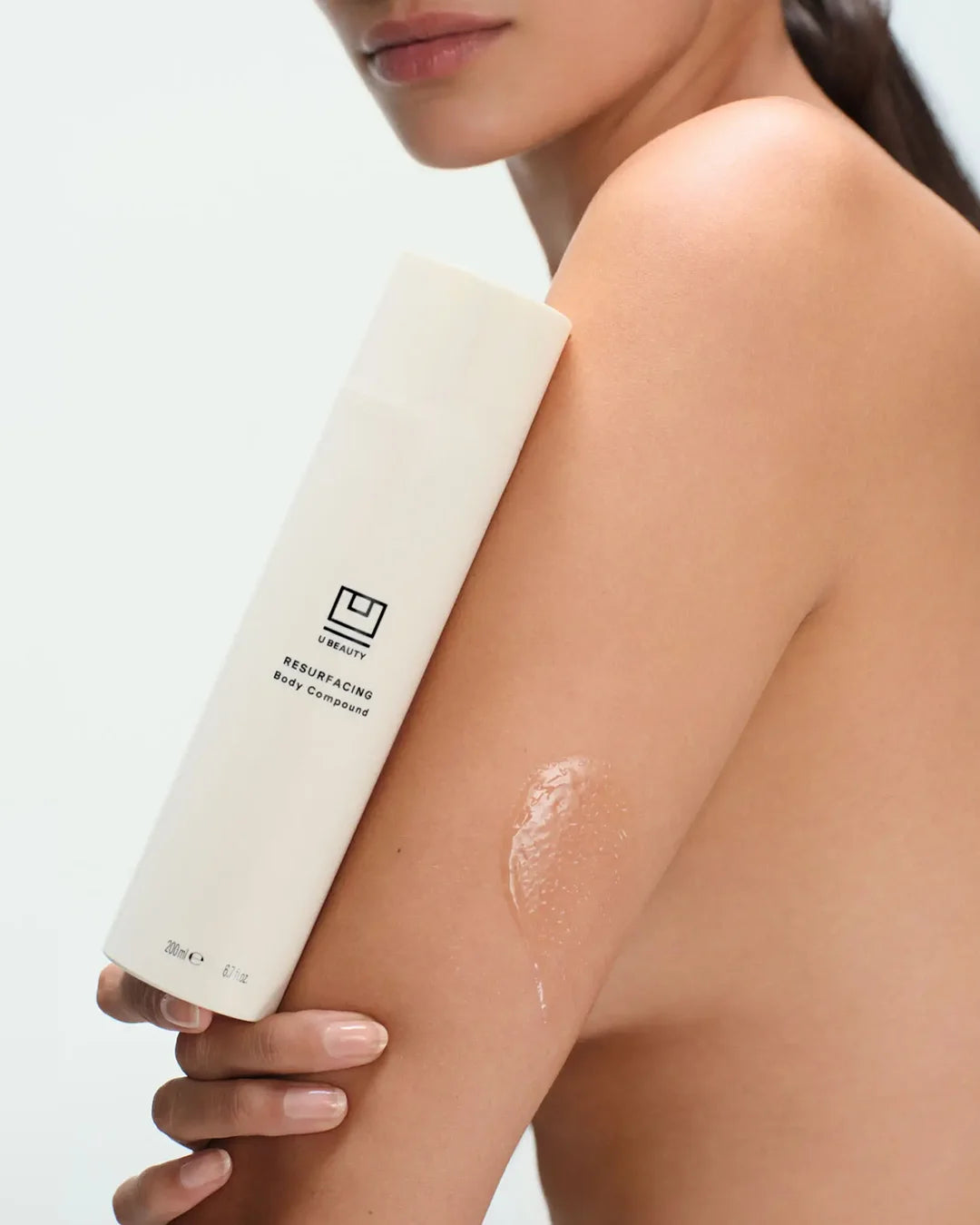 Person applying a white bottle of lotion to their arm with a visible brand logo.