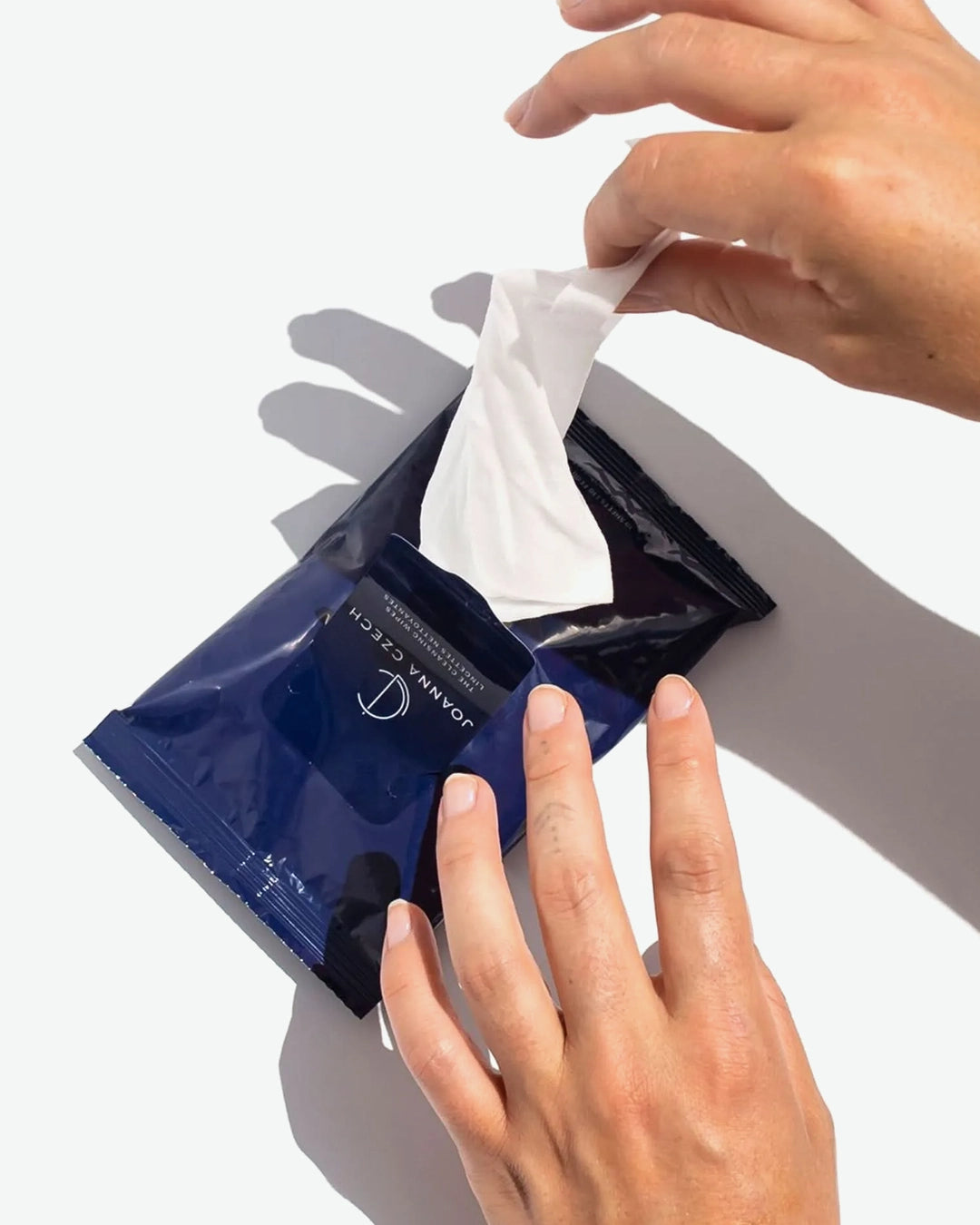 Person taking a white wipe from a blue package labeled 'Joanna Czech' on a light gray background
