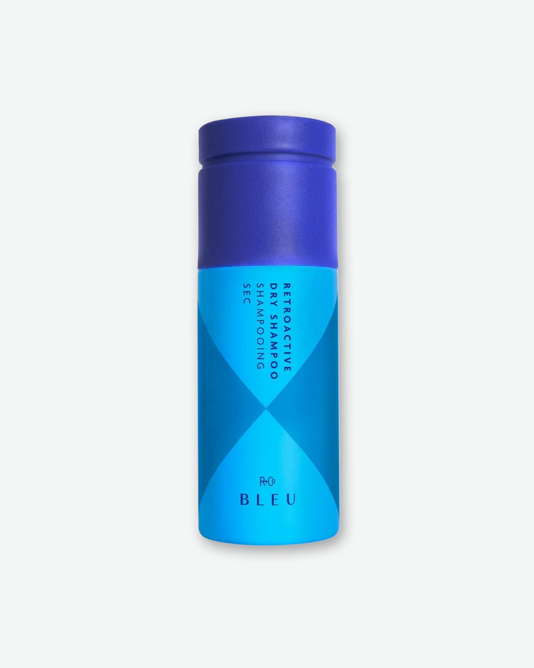 A bottle of R+Co BLEU Retroactive Dry Shampoo. The cylindrical spray can features a deep royal blue cap and a lighter cyan blue body with a dark blue geometric hourglass pattern, set against a plain light gray background.