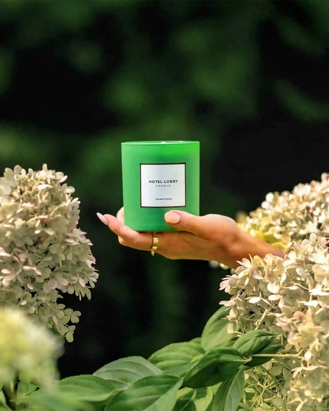 Hand holding a green candle with a white label among flowers