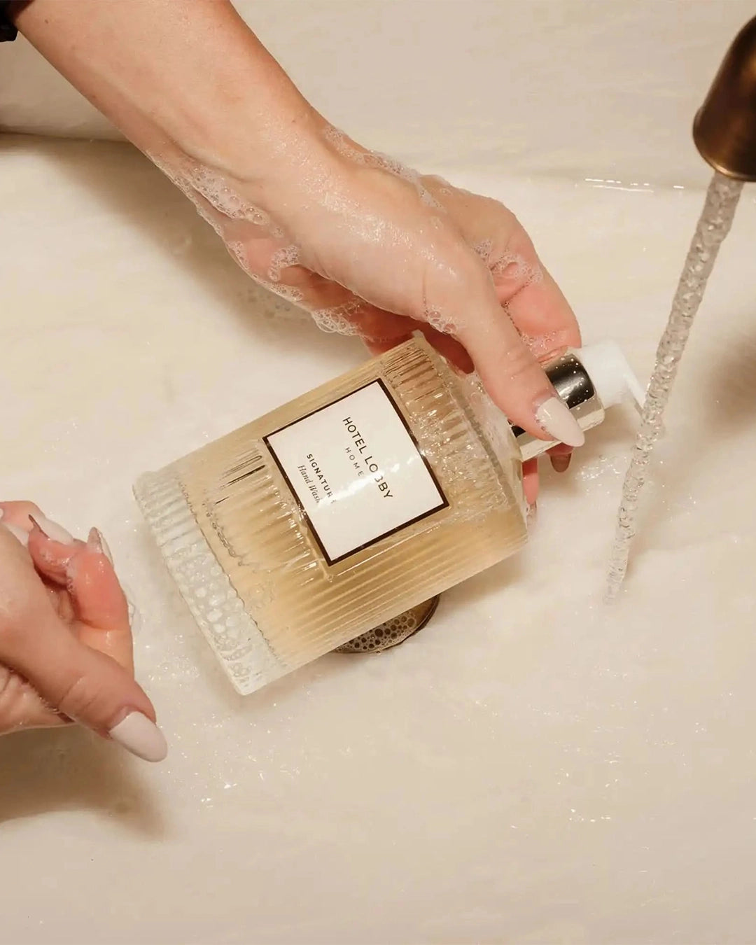 Person holding a bottle of soap with a brush over a sink