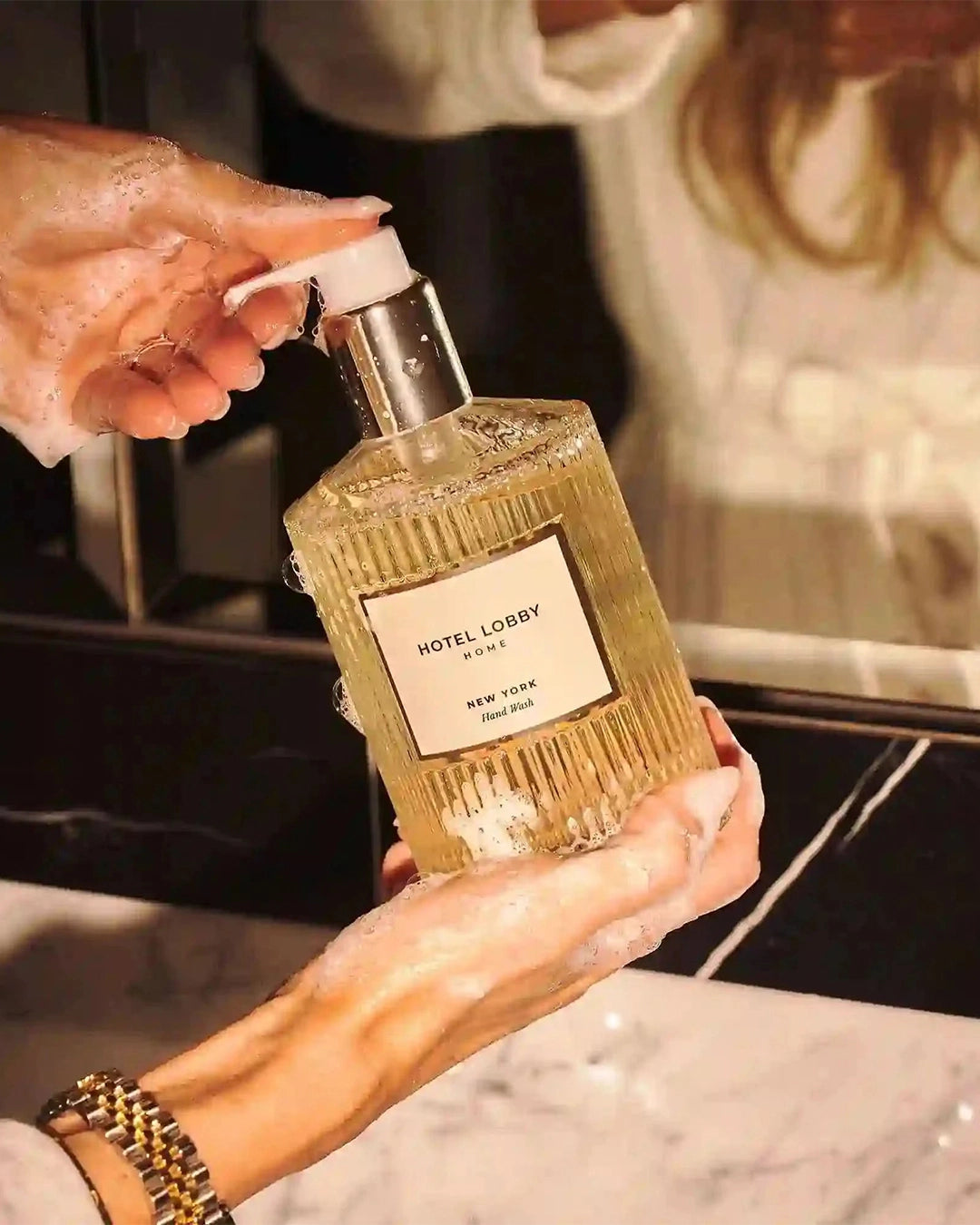 Hand holding a gold bottle labeled 'HOTEL LOBBY' with soap suds.