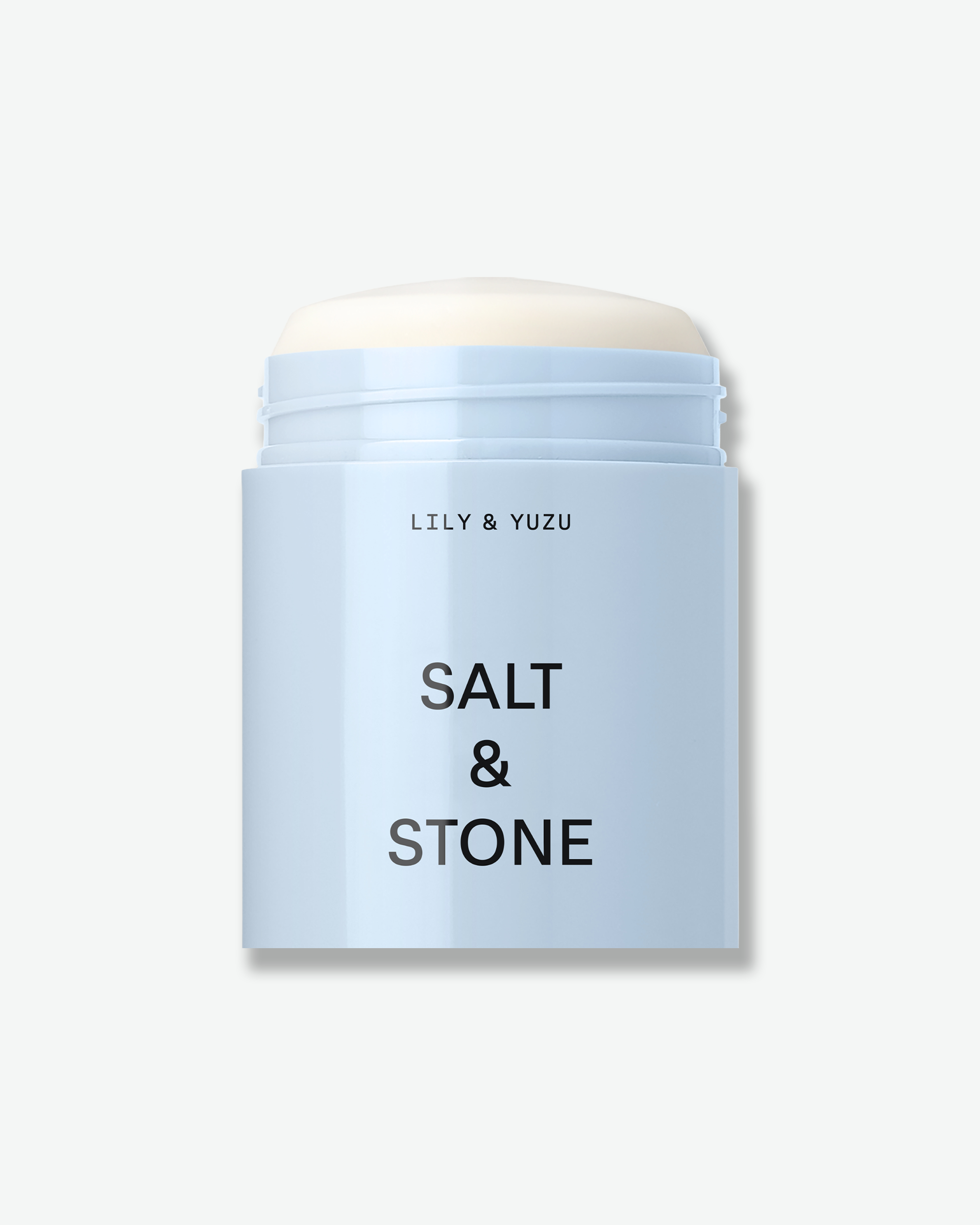 An open, light blue container of Salt & Stone "Lily & Yuzu" deodorant stick showing the product inside against a white background.