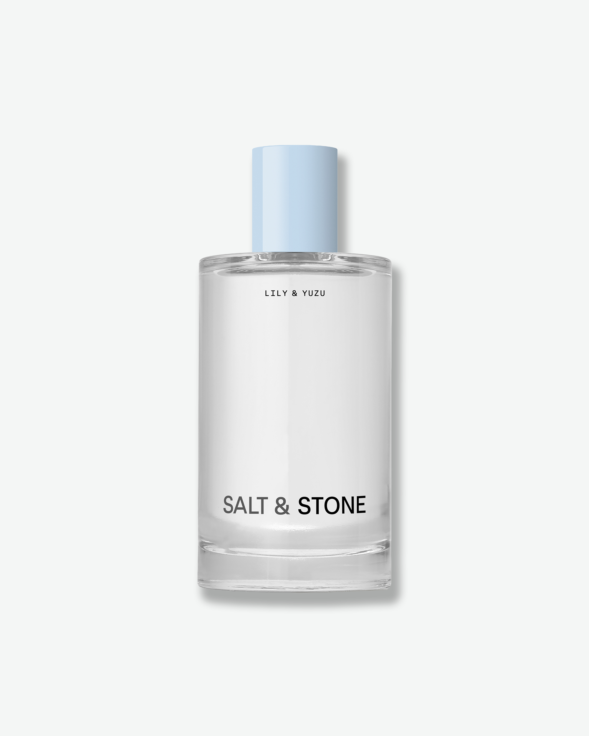Clear glass bottle of Salt & Stone "Lily & Yuzu" fragrance with a light blue cap against a white background.
