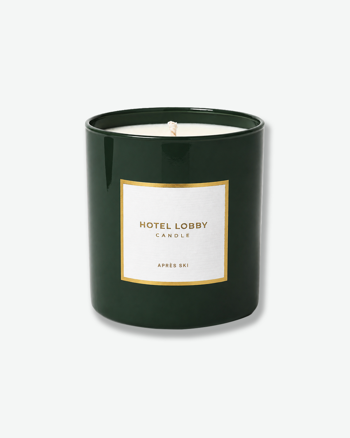 Hotel Lobby Candle Après Ski scented candle in a glossy forest green glass vessel with white wax and a gold-trimmed label.