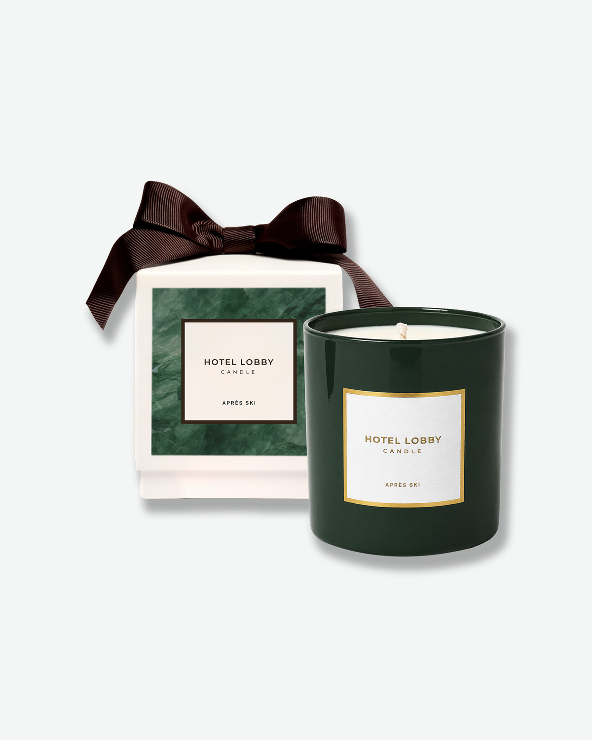 Hotel Lobby Candle Après Ski scented candle displayed alongside its green and cream gift box, finished with a dark brown ribbon bow.