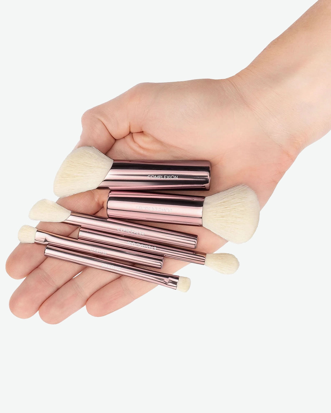 Set of rose gold makeup brushes held in a hand against a white background