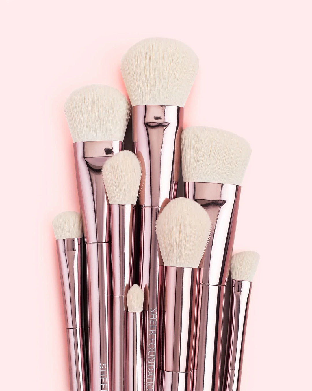 Set of rose gold makeup brushes with white bristles on a pink background