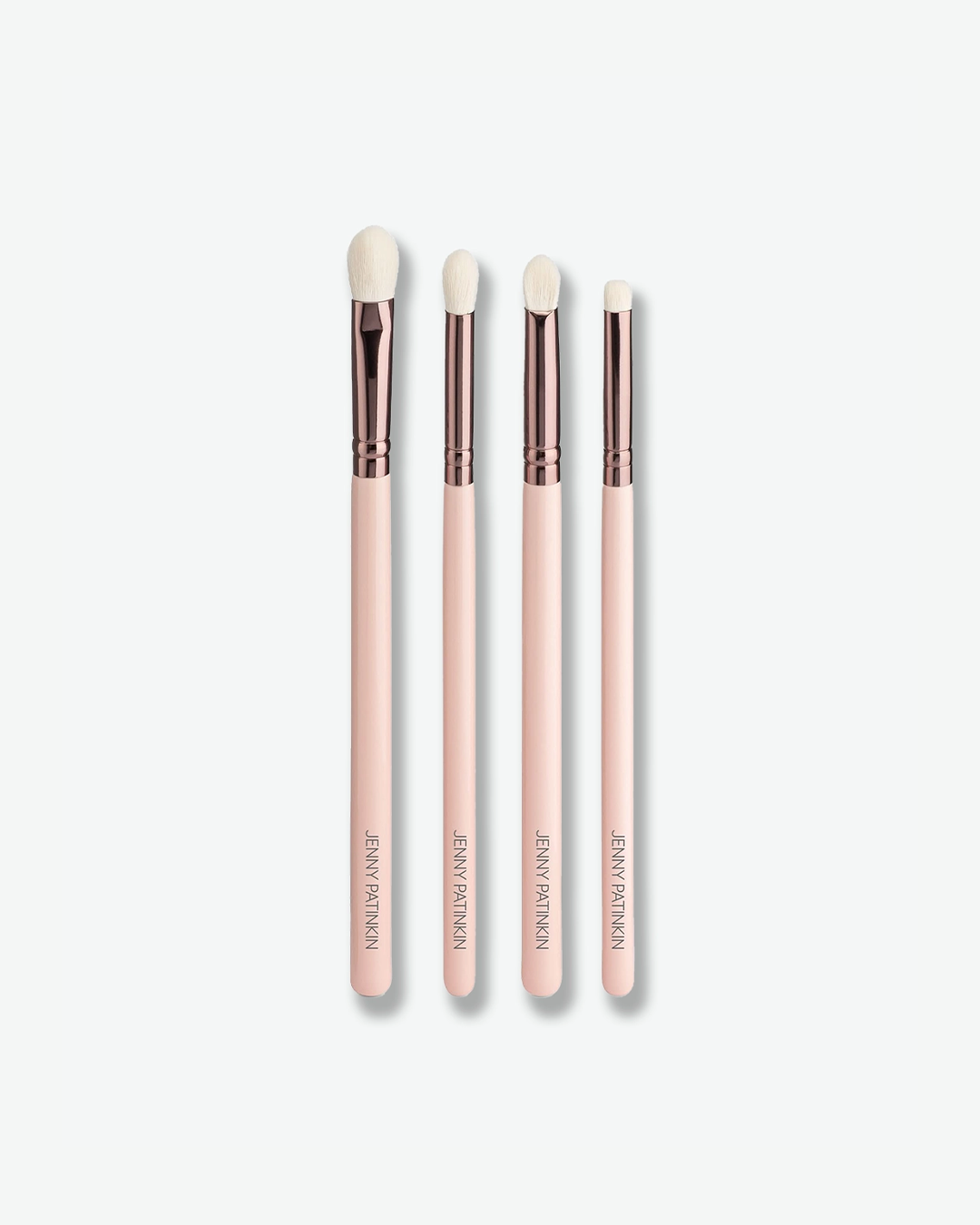 A product shot of four slender eye makeup brushes arranged vertically against a plain light gray background. Each brush has a light pink handle with "JENNY PATINKIN" stamped in gold at the bottom, a metallic rose-gold ferrule, and fine white bristles tailored for detailing, blending, and shading.