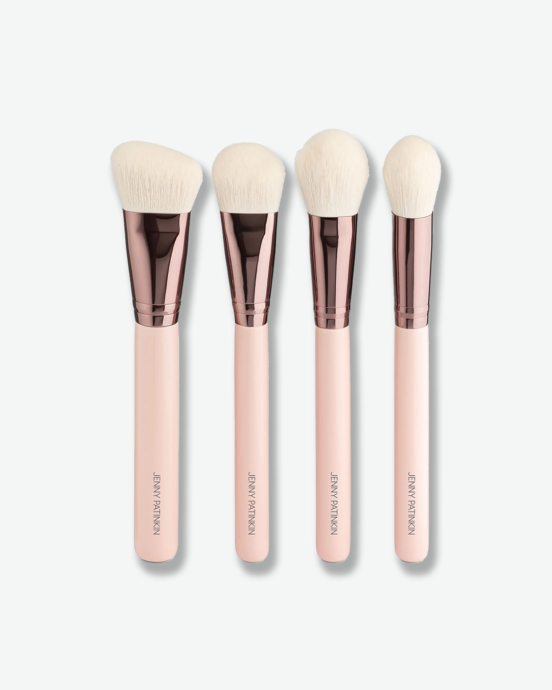 A product shot of four complexion makeup brushes lined up vertically against a plain light gray background. The brushes have light pink handles featuring gold lettering, glossy rose-gold ferrules, and soft white bristles shaped into distinct angles and domes for contouring, foundation, and powder application.