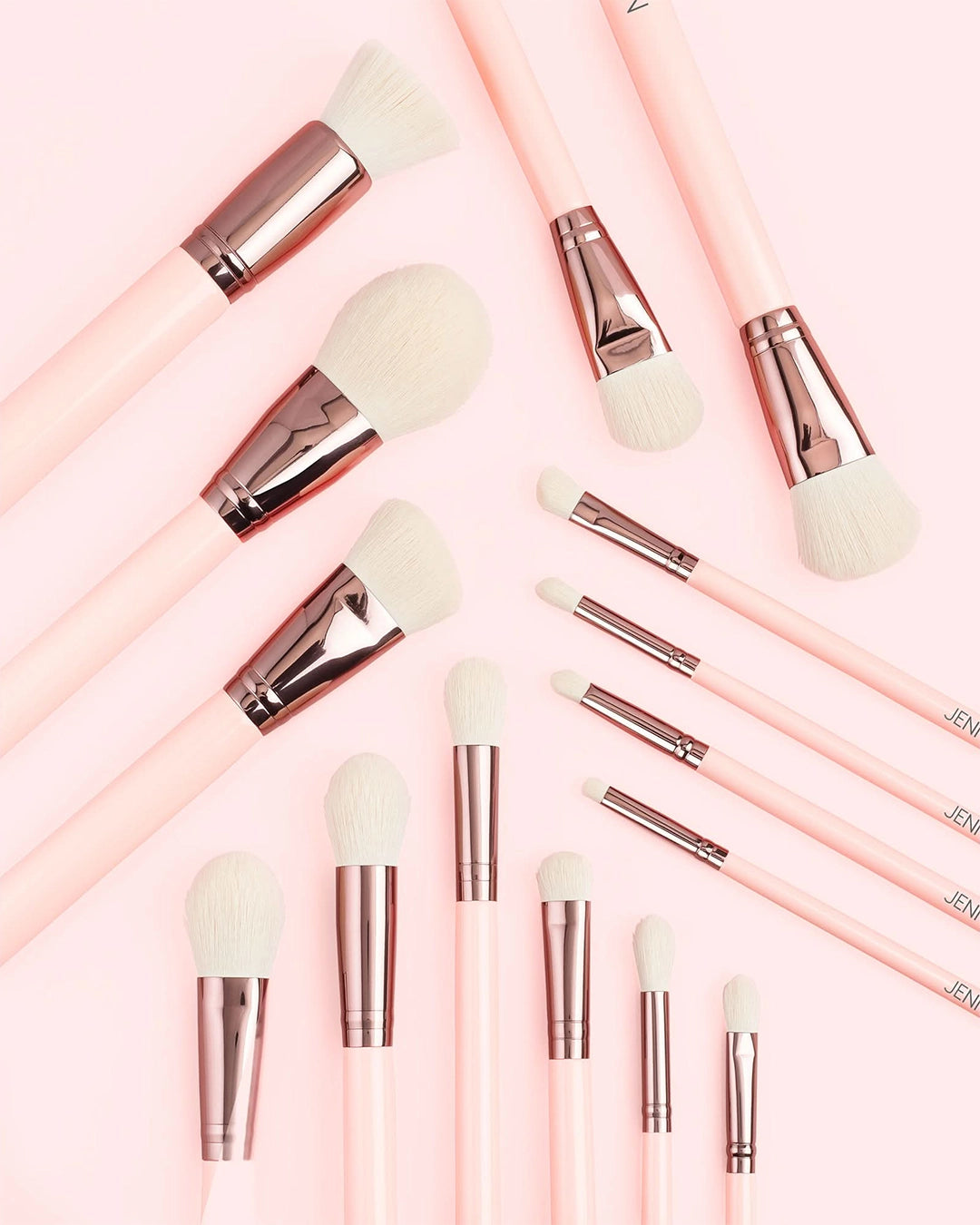 Makeup brushes with pink handles and silver ferrules on a light pink background