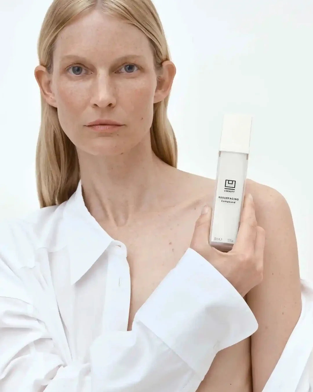Woman holding a skincare bottle with a plain background