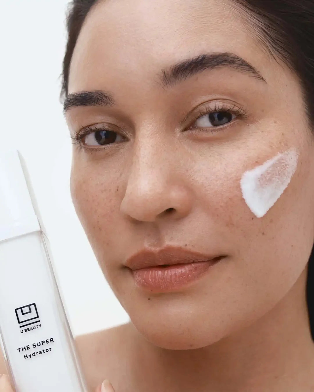 Woman applying skincare product with 'U Beauty' bottle in the background