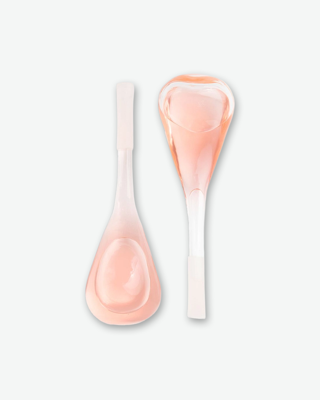 A product shot of two glass facial cryo globes filled with a translucent pink liquid, arranged vertically next to each other on a plain light gray background. The globe on the left is positioned with its wide, tear-shaped cooling bulb facing down and its frosted white handle pointing up. The globe on the right is inverted, with its wide cooling bulb at the top and its handle pointing down.