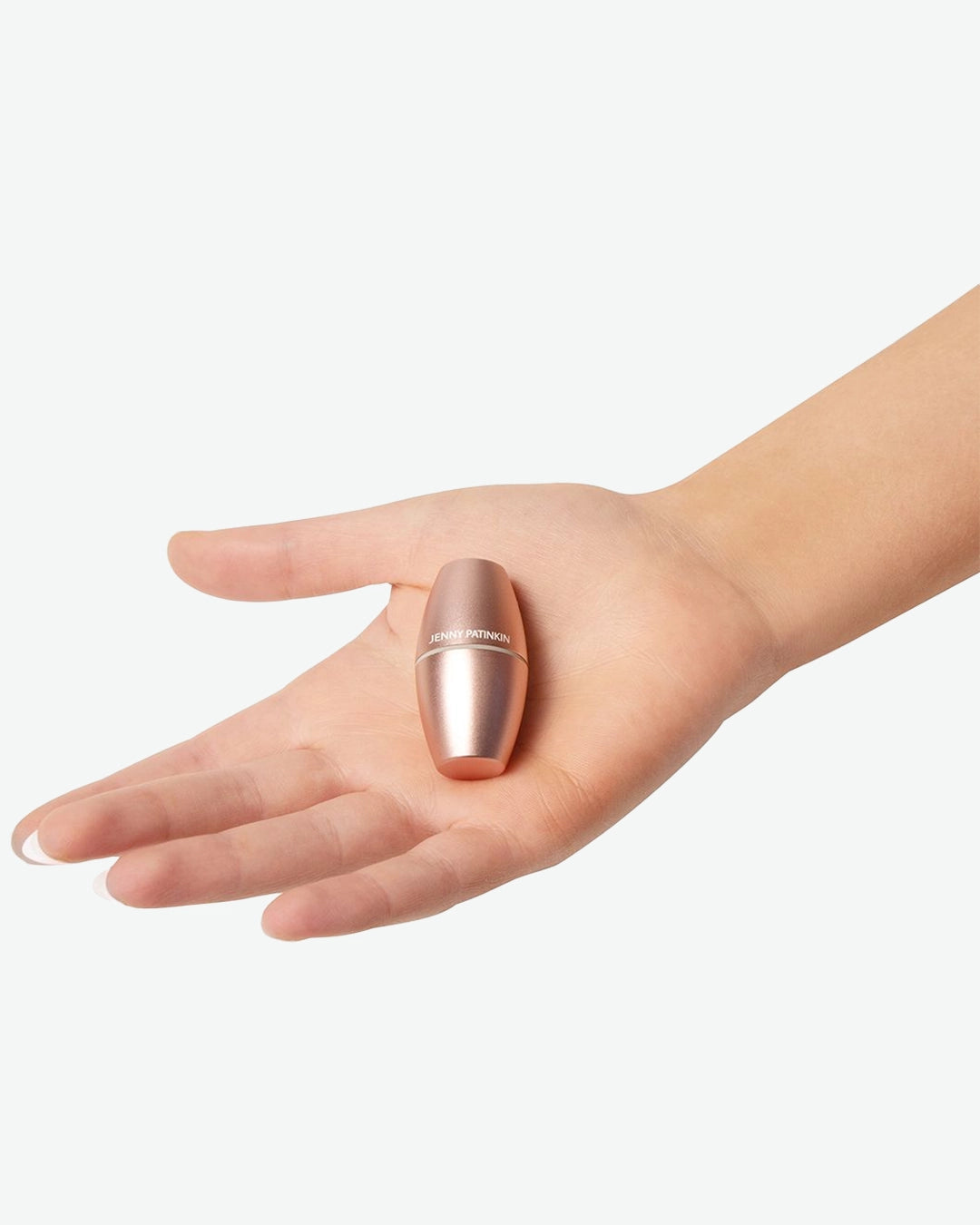 The Jenny Patinkin Blotter Baby Mattifying Roller rests in the palm of a hand against a light gray background. The compact rose-gold tool is small enough to fit comfortably in the hand, highlighting its portable, travel-friendly design. Designed to absorb excess oil and reduce shine, the reusable roller offers a quick way to refresh the skin throughout the day without disturbing makeup.