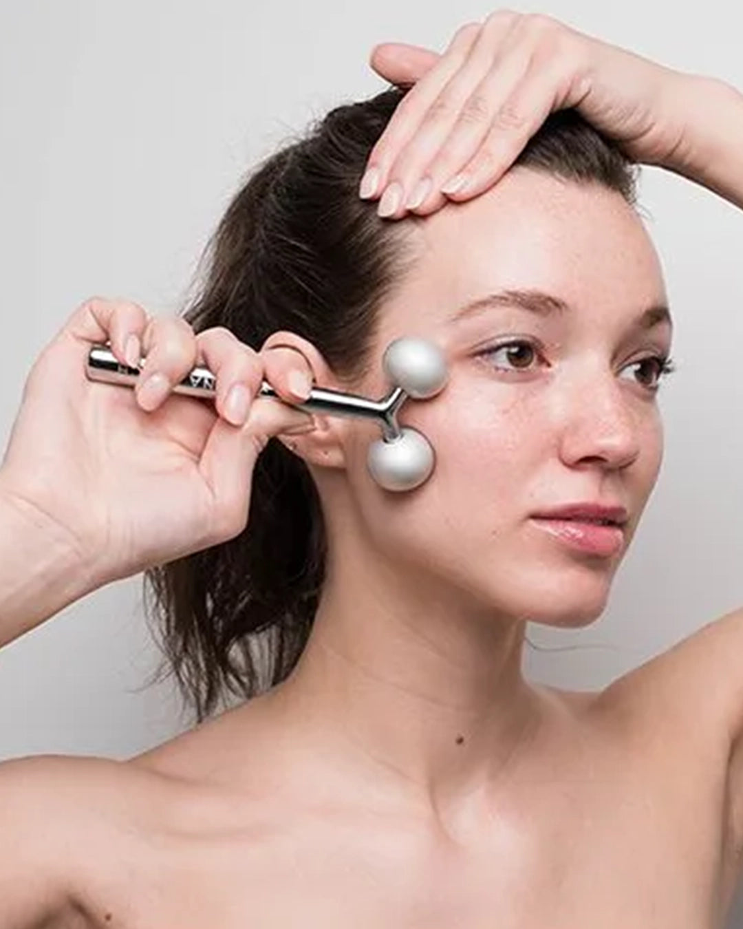 Woman using a facial roller on her face against a plain background