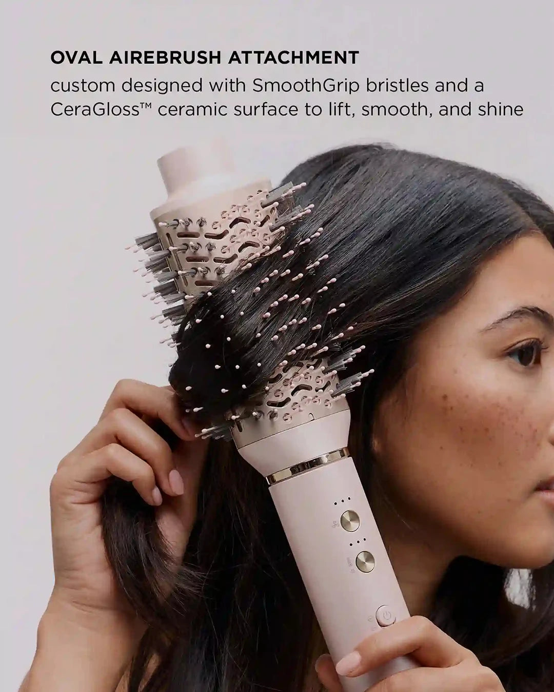 Person using a hair styling tool with an oval airebrush attachment on a plain background
