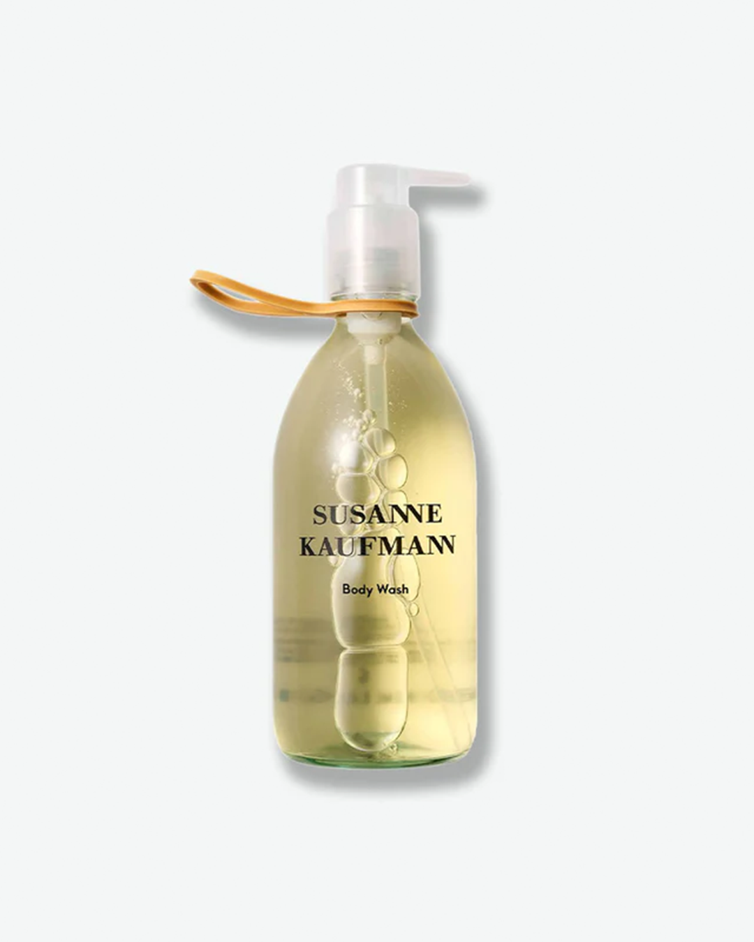 A product shot of a Susanne Kaufmann Body Wash bottle, centered against a plain light gray background. The clear glass bottle holds a translucent, pale green-yellow gel with visible air bubbles around the interior tube. It features a clear pump dispenser with a tan rubber band or loop attachment secured around its neck.