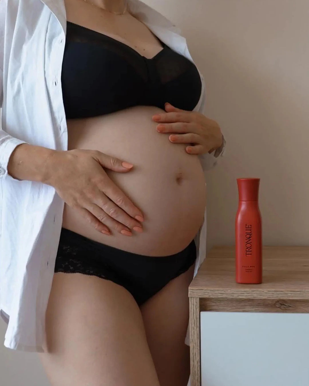 Person wearing black underwear with a red bottle labeled 'TRONQUE' on a wooden surface.