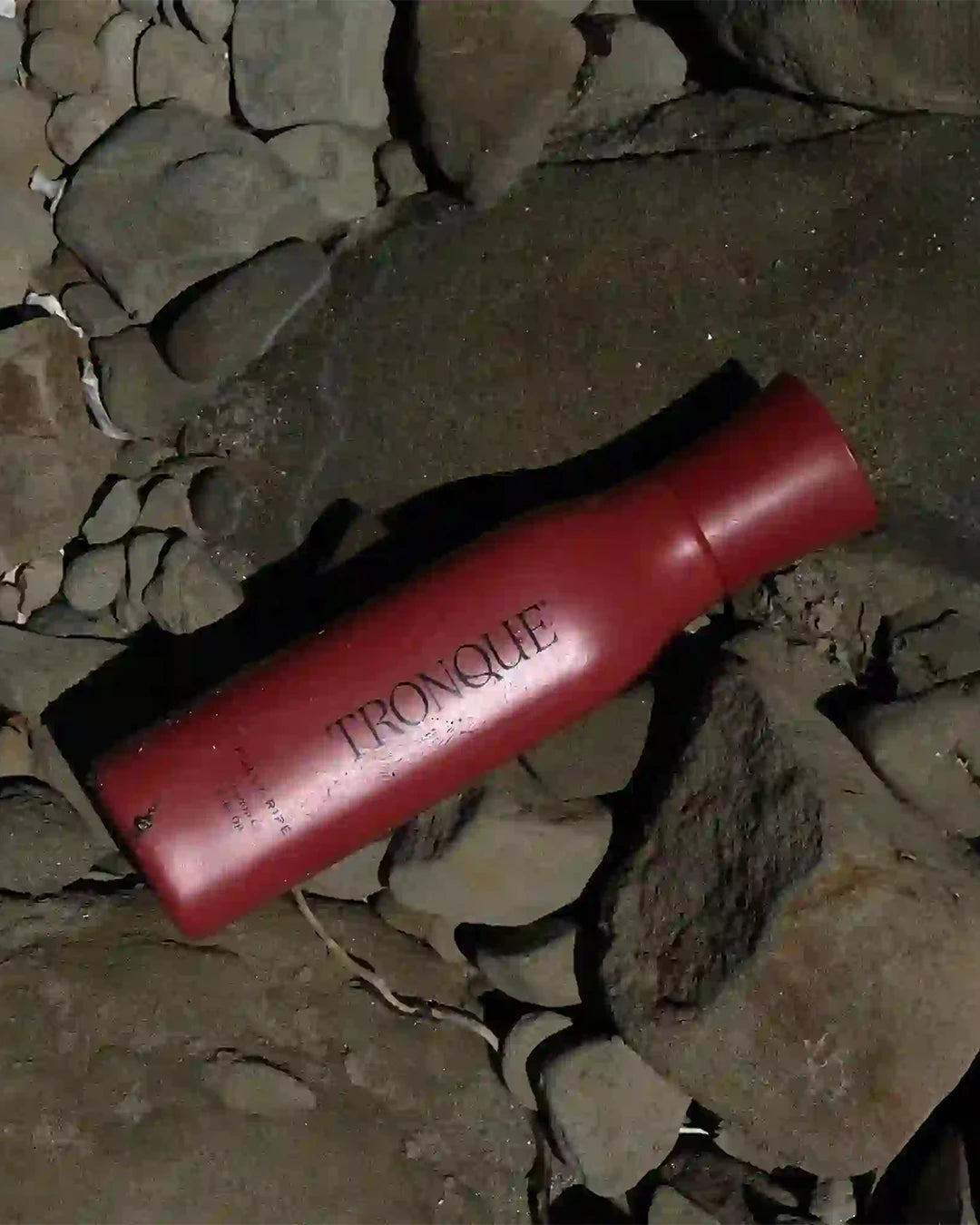 Red bottle with 'Tronque' branding on a rocky surface