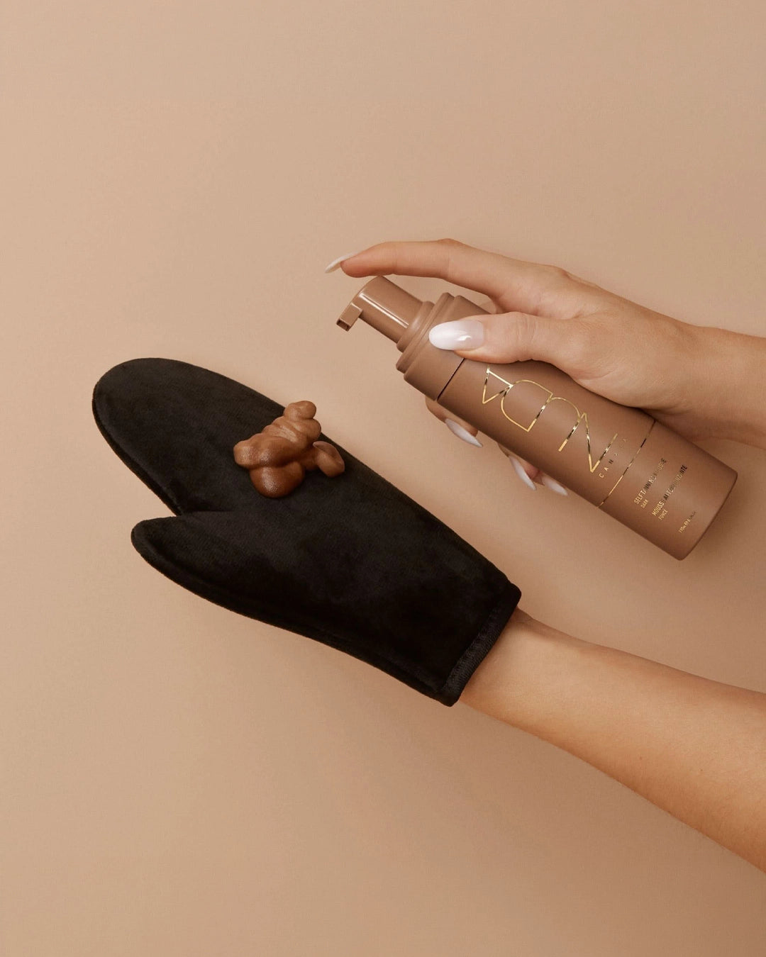 Person using a brown spray bottle on a black glove against a beige background