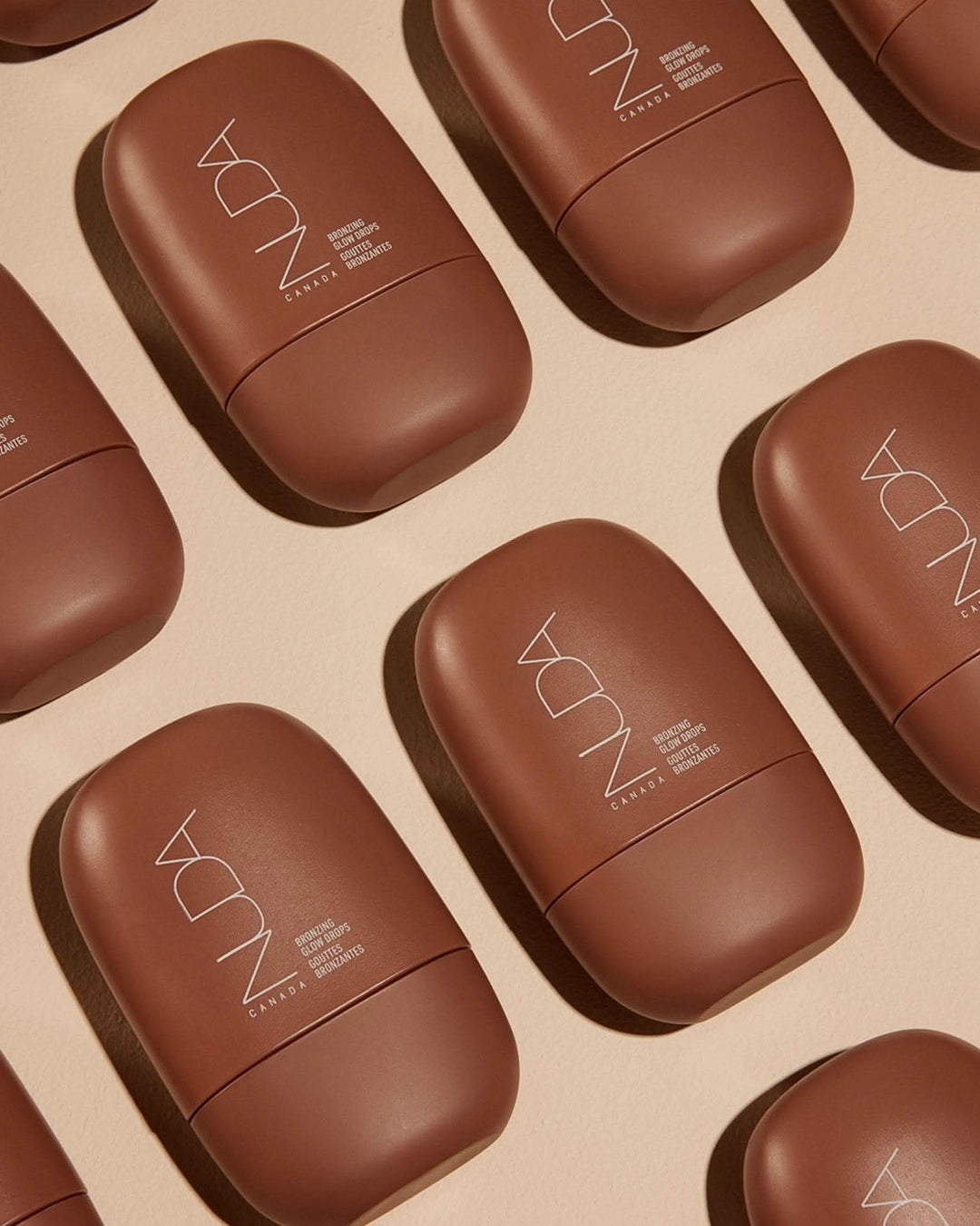 Multiple brown cosmetic containers with 'NUDA' branding on a beige background
