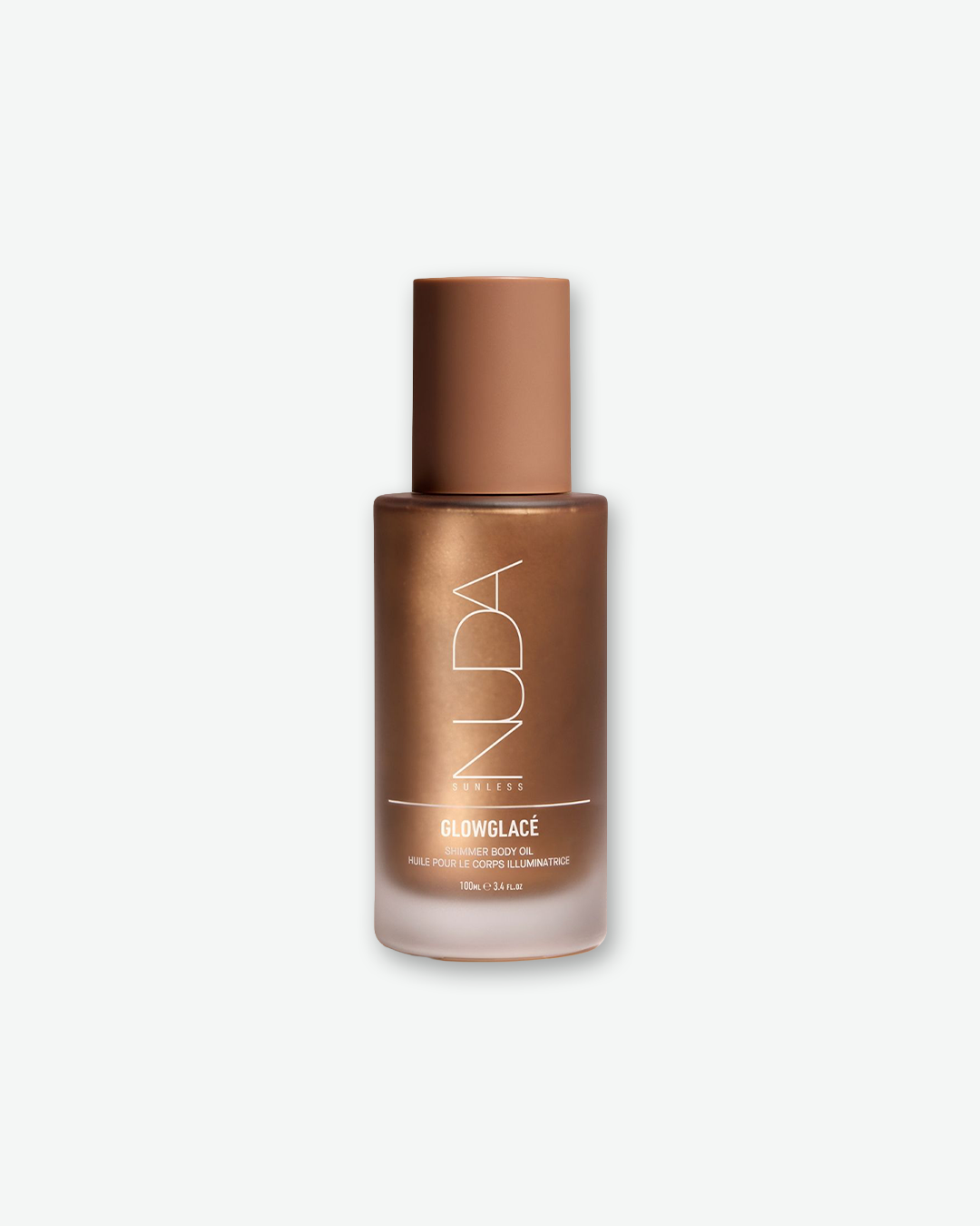 A product shot of a NUDA Glowglacé Shimmer Body Oil bottle, centered against a plain light gray background. The cylindrical frosted glass bottle reveals a shimmering, metallic bronze-colored oil inside and is topped with a smooth, matte tan cap. The front features the "NUDA" brand name printed vertically in a thin white outline font above the white text "GLOWGLACÉ SHIMMER BODY OIL", its French translation, and the volume "100ml e 3.4 Fl.Oz".