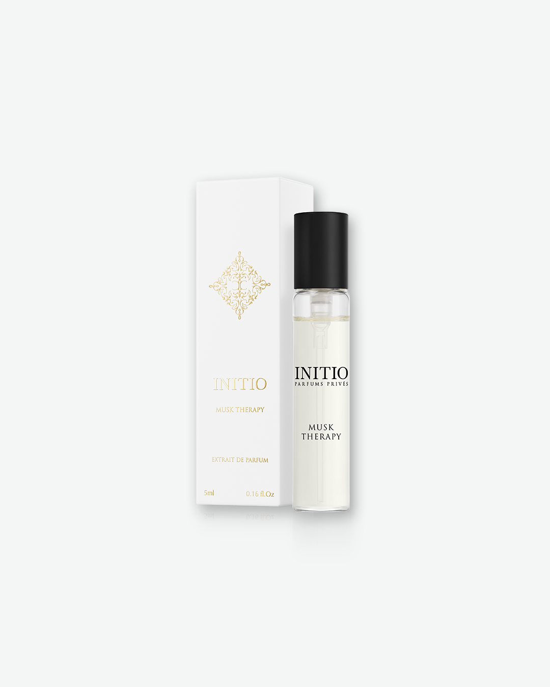 An Initio Parfums Privés "Musk Therapy" Extrait de Parfum travel size sample. A slender, clear glass spray vial with a black cap sits upright next to its vertical white packaging box. The box features an elegant, symmetrical gold filigree emblem at the top, with the brand name "INITIO" and "MUSK THERAPY" printed in gold lettering.