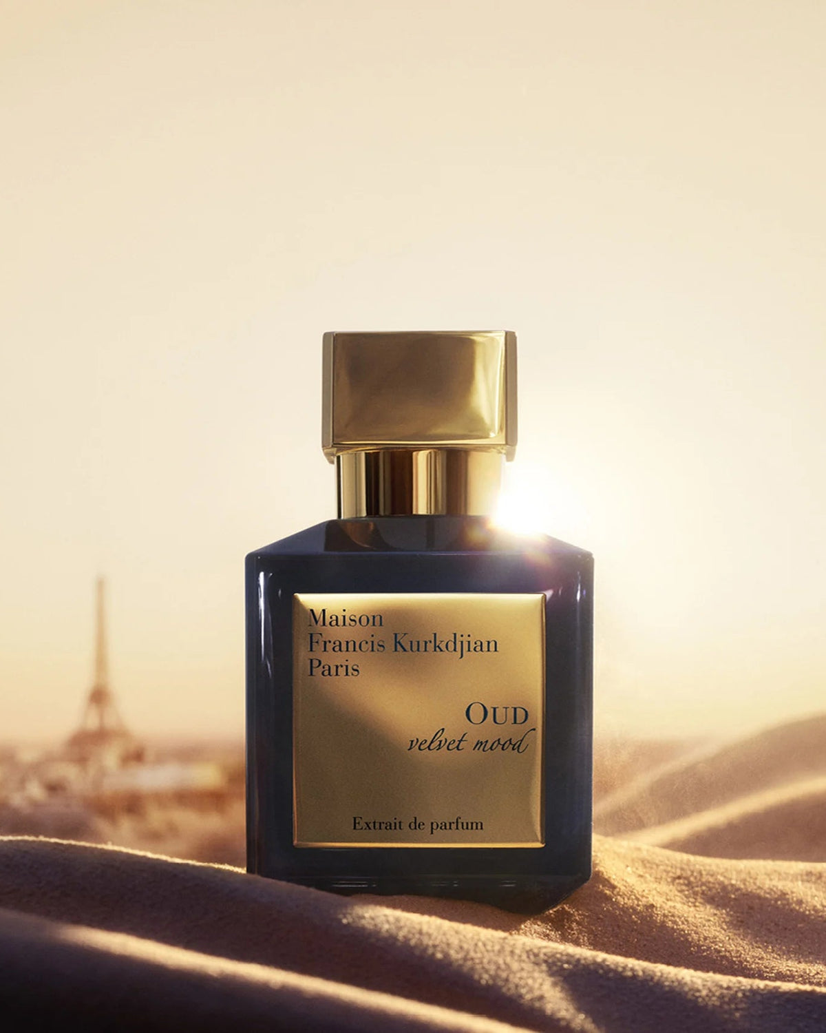 Maison Francis Kurkdjian Oud Velvet Mood Extrait de Parfum bottle set against a softly blurred Paris skyline at golden hour, with warm sunlight reflecting off the gold accents.