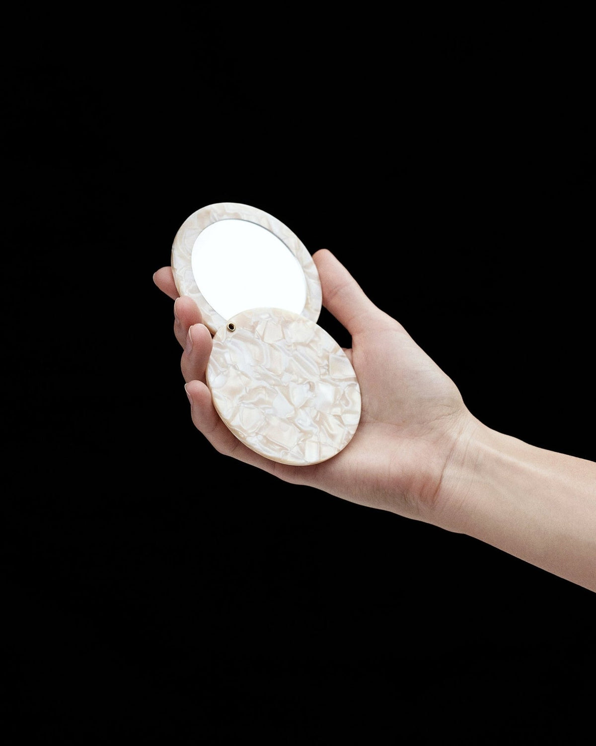 Hand holding a round, light-colored compact mirror against a black background