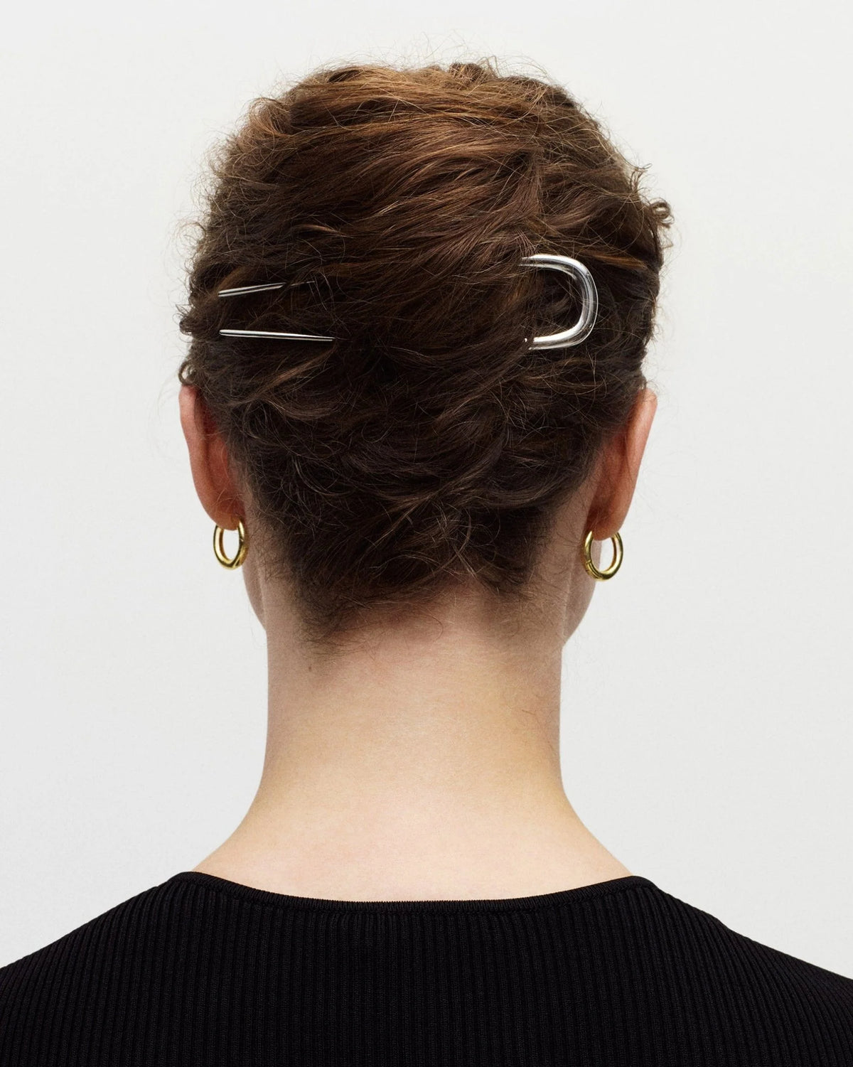 Person with hair styled in an updo using two silver hair clips on a plain background