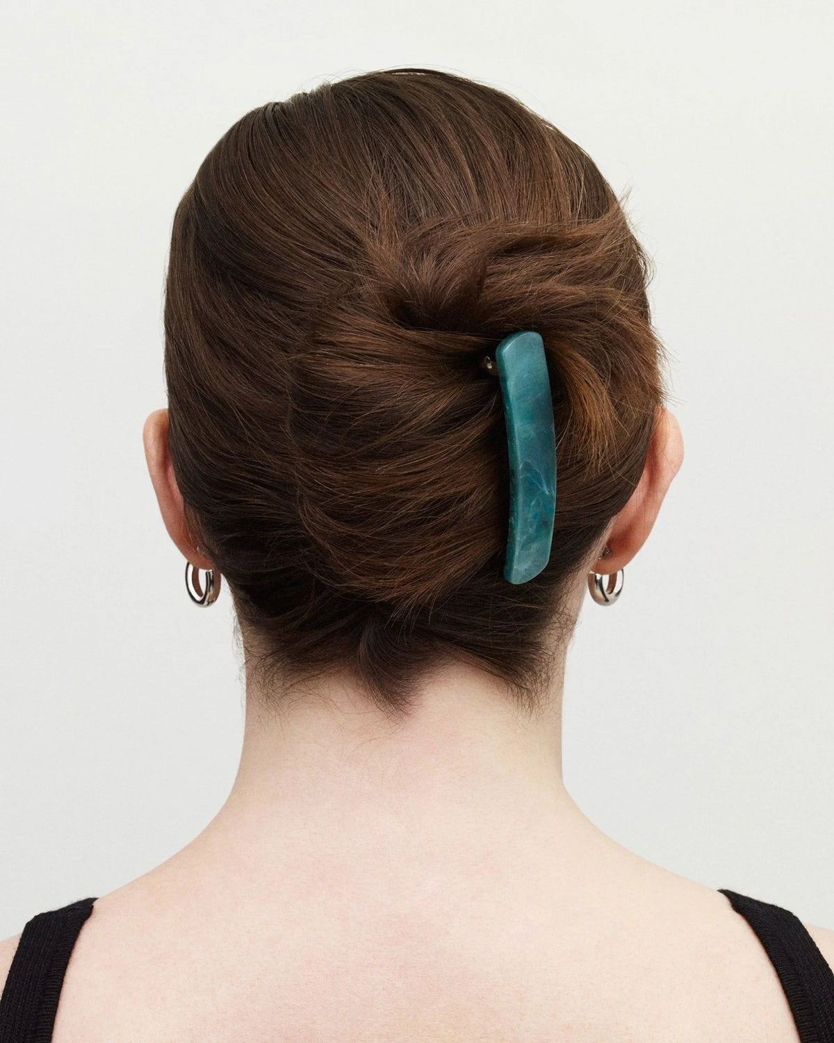 Person with a teal hair clip in their bun against a plain background