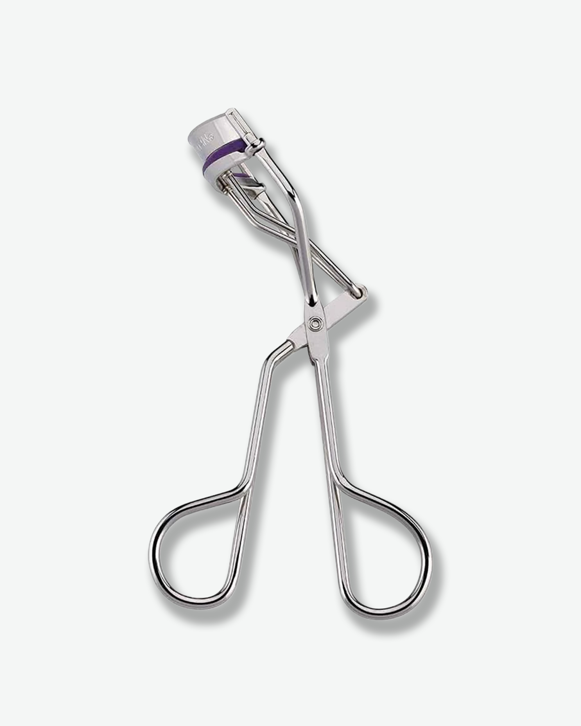 Front view of a classic silver metallic Tweezerman eyelash curler standing against a plain gray background, featuring scissor-like handle loops and a purple silicone cushioning pad along the upper curling bar.