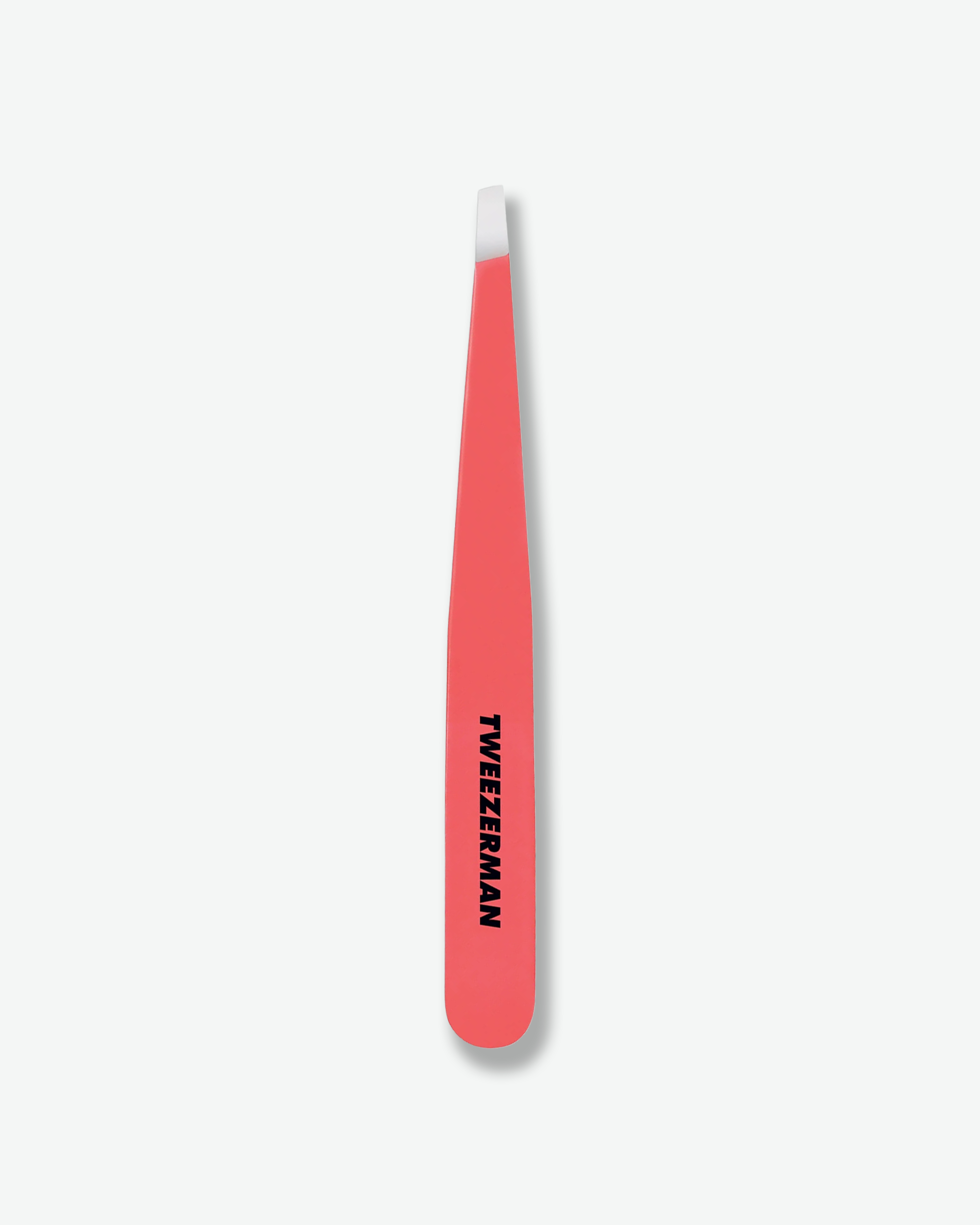 Front view of a pair of classic Tweezerman slant tweezers positioned vertically against a plain gray background. The tool features a vibrant coral pink finish with the brand name printed vertically in black, terminating in sharp, hand-filed silver metallic tips.