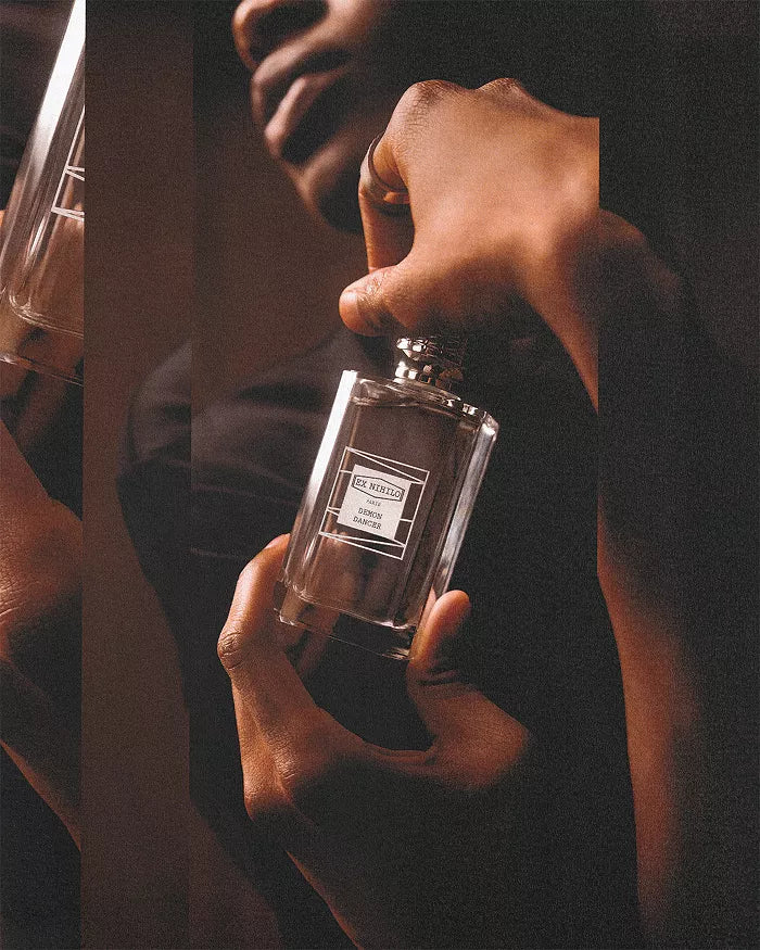 Close-up of hands holding a Ex Nihilo Demon Dancer bottle against a dark, moody background with warm, grainy lighting.