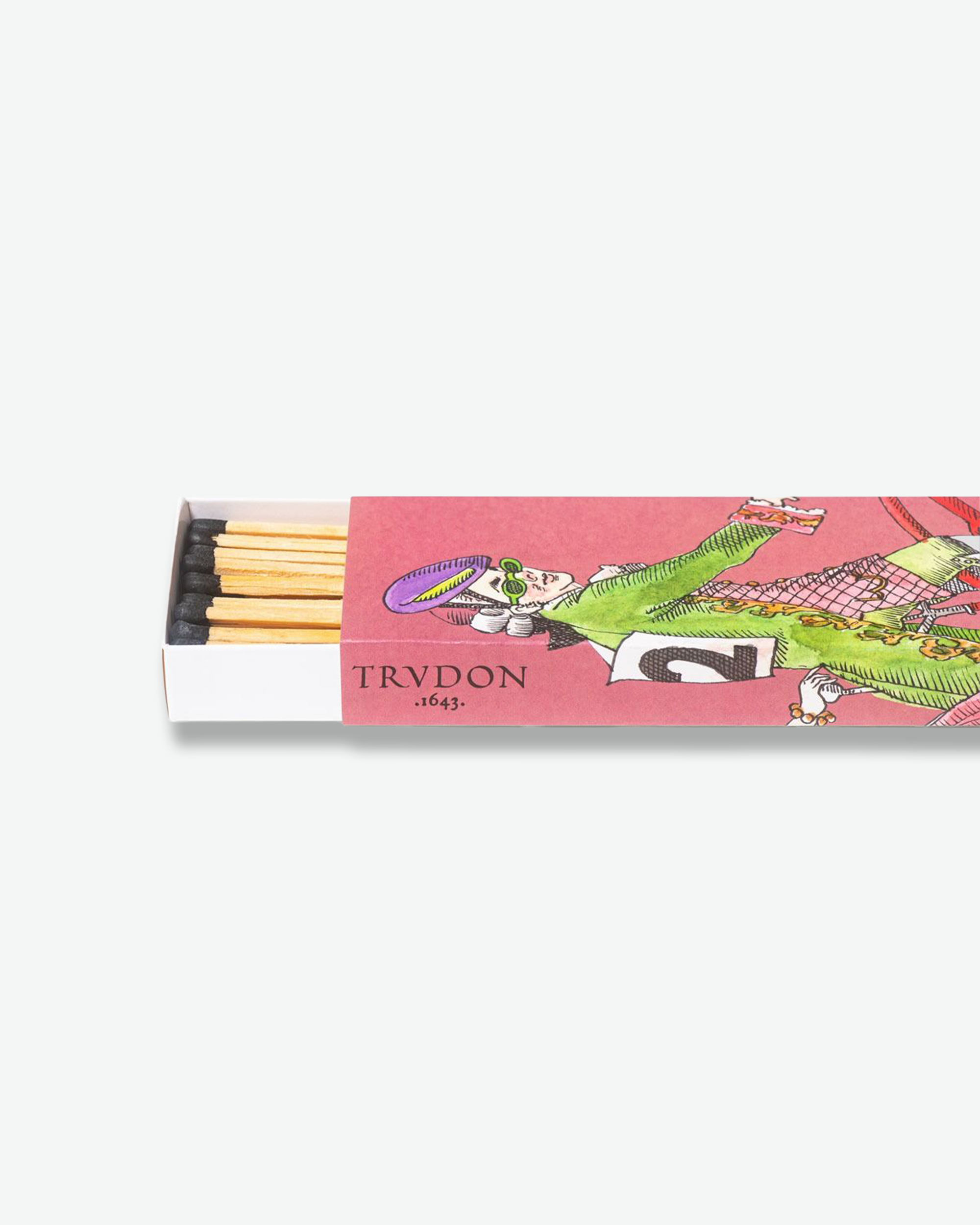 A close-up, horizontal view of a pink Trudon matchbox partially slid open to reveal black-tipped wooden matches inside. The box displays the brand name "TRVDON .1643." and a whimsical illustration of an 18th-century man wearing green sunglasses and a purple hat.