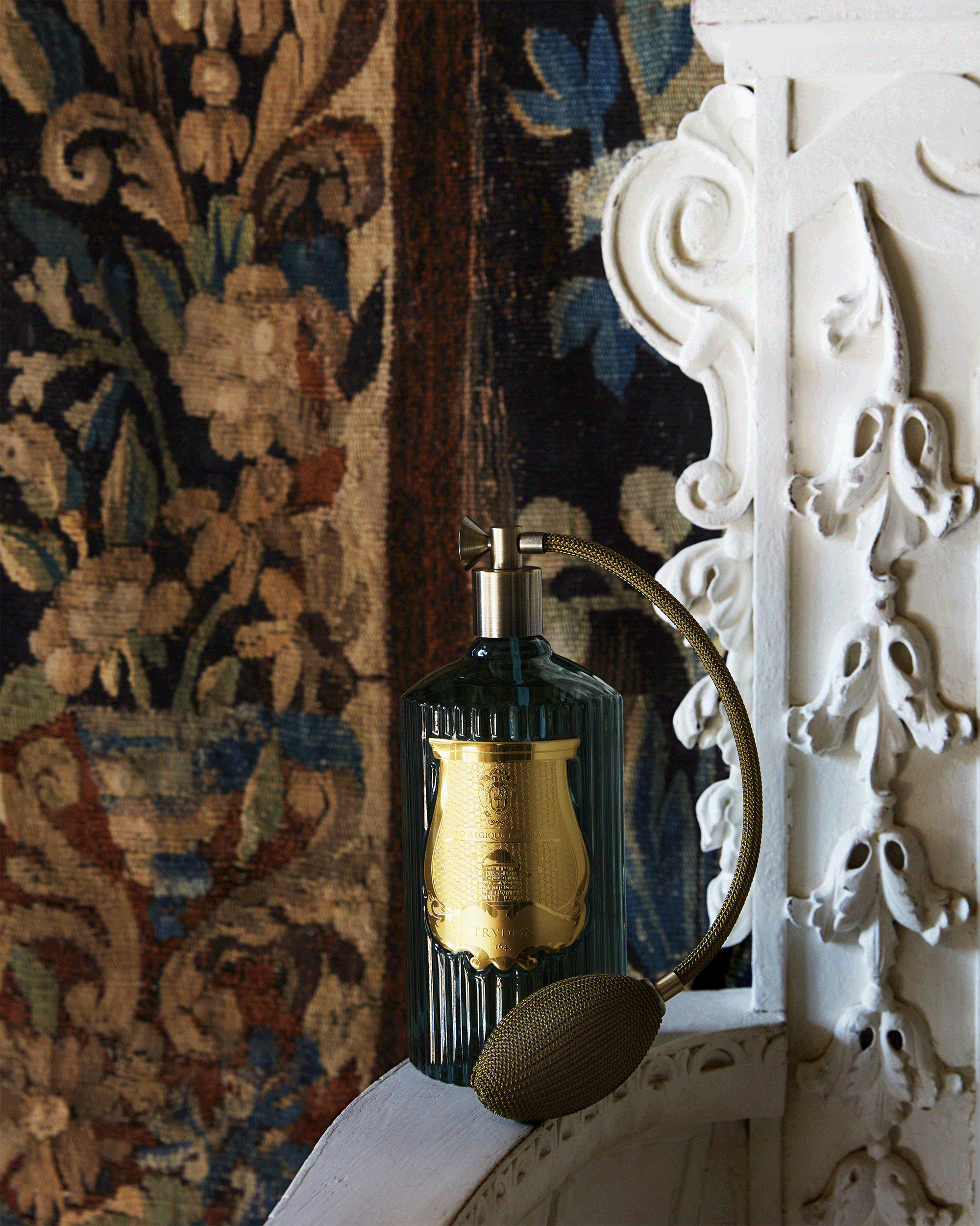 Decorative bottle with gold cap on a white ornate surface with a patterned rug in the background