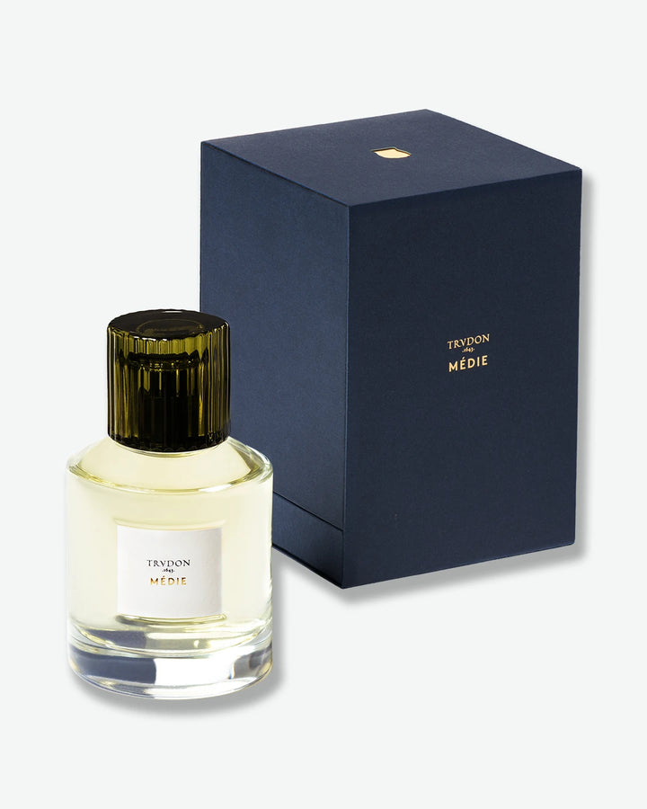 A heavy glass bottle of Trudon Médie Eau de Parfum standing next to its elegant, deep navy blue presentation box.