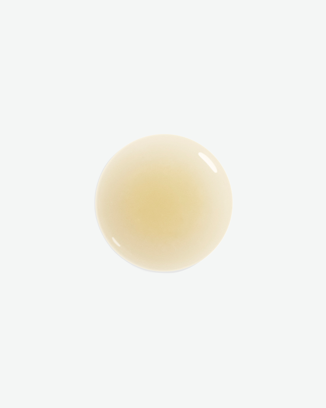 A single round drop of clear, light yellow liquid skincare treatment texture isolated on a white background.